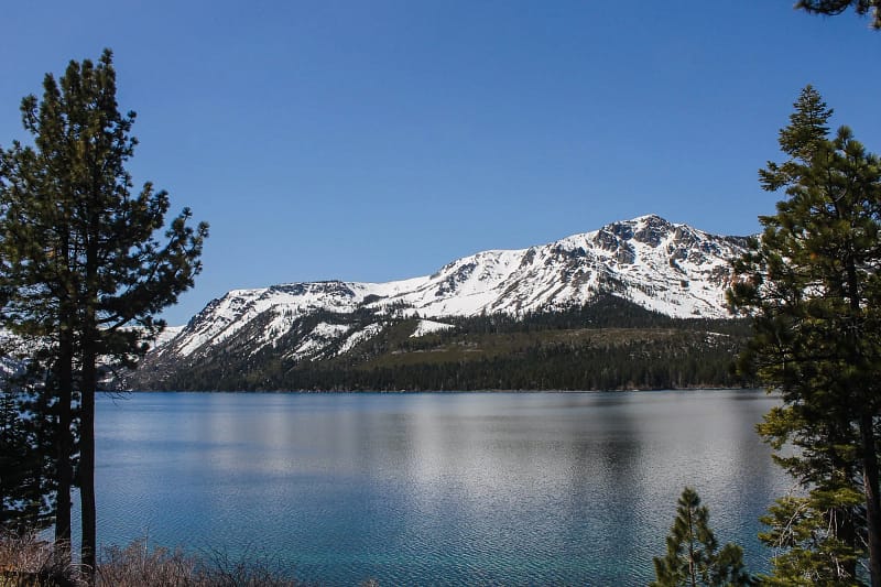 view of the crystal clear blue waters of Lake Tahoe surrounded by snow-capped mountains.
